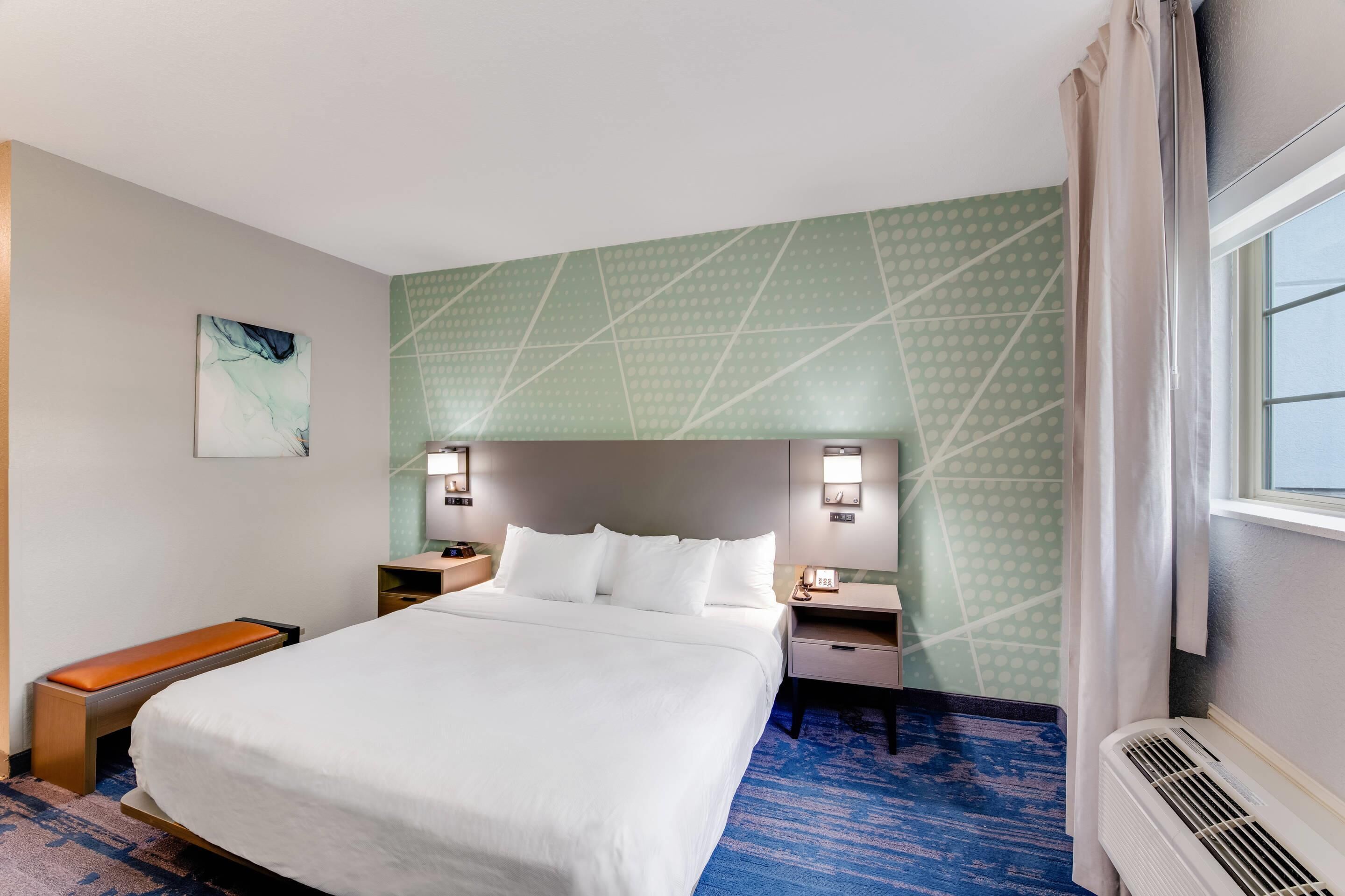 A hotel room with a large bed, two bedside tables, a bench, and a window with curtains.