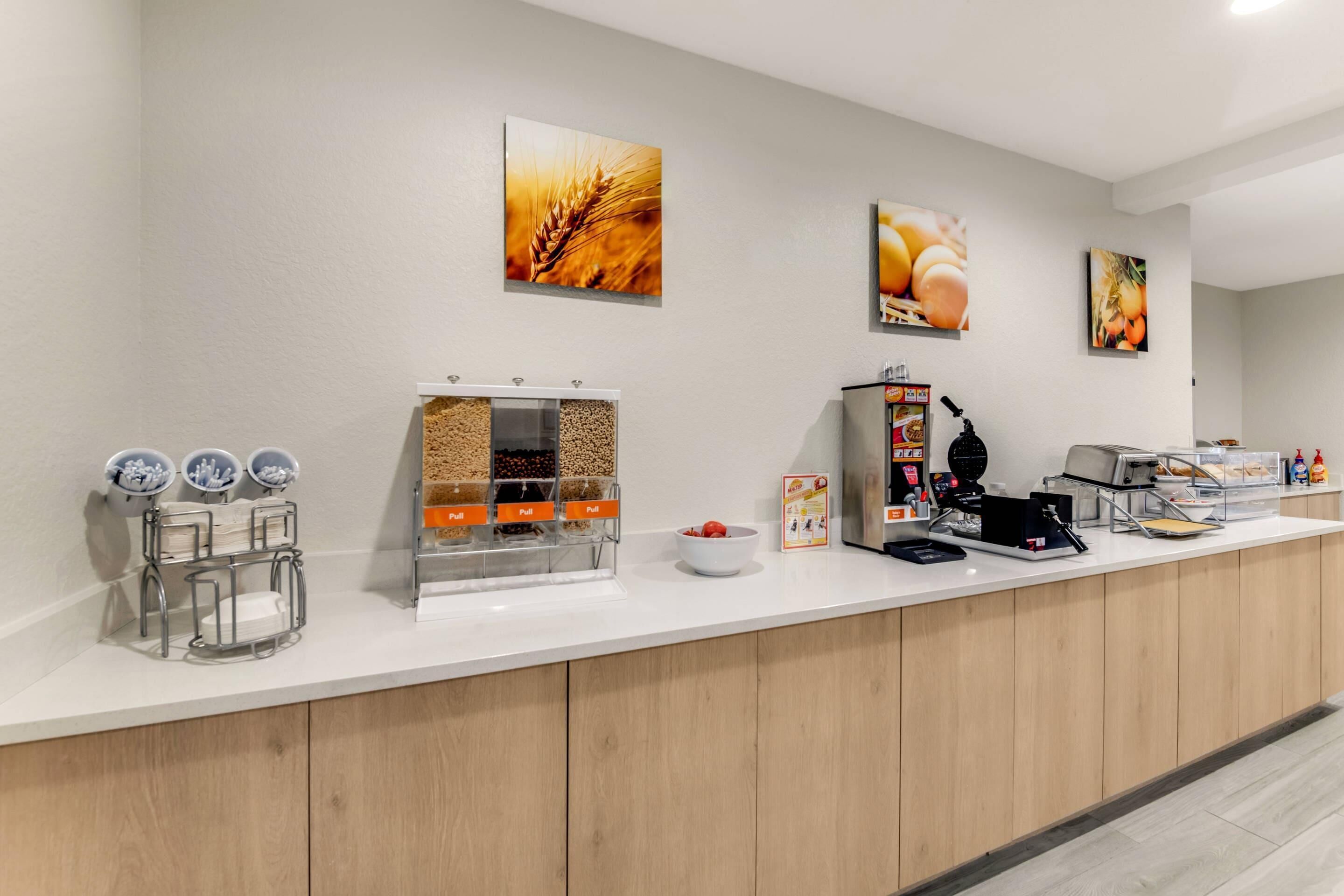 Een ontbijtbuffet met een koffieapparaat, cornflakesautomaten en een schaal fruit.