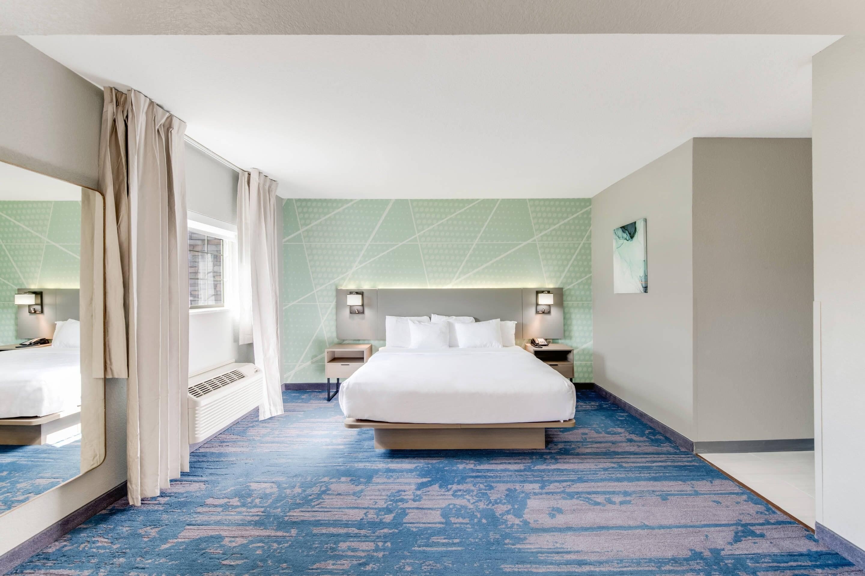 Une chambre d’hôtel avec un grand lit, des tables de chevet, un miroir et une fenêtre avec des rideaux.