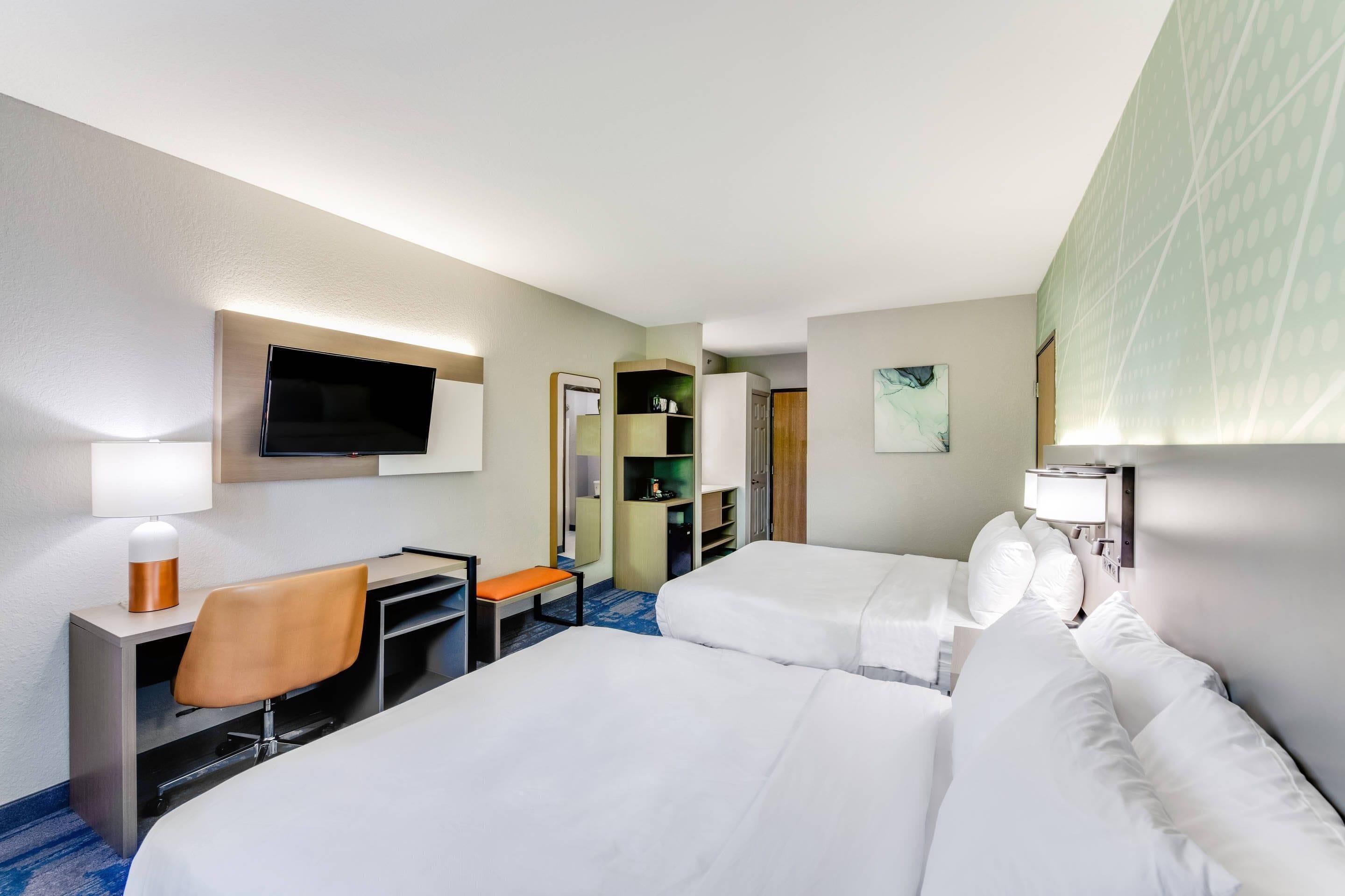 A hotel room with two beds, a desk with a chair, a TV, and a wardrobe.