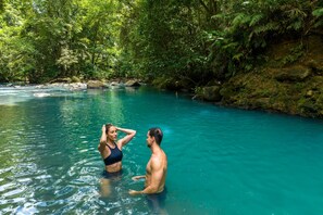 A couple in a natural, clear water setting surrounded by lush greenery.