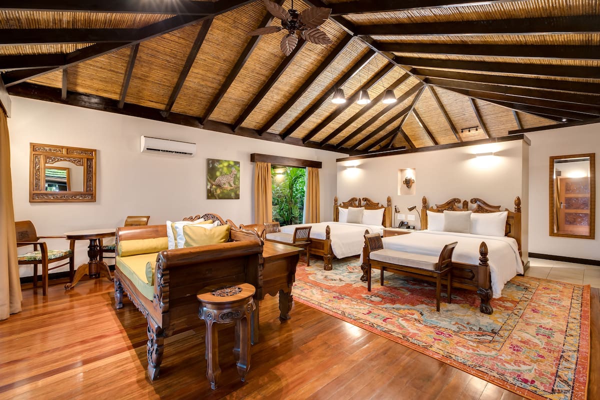 A room with a wooden ceiling, a bed with white bedding, a wooden sofa, a small table, and a colorful rug.