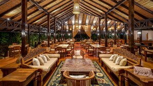 A spacious indoor area with wooden furniture, a high ceiling with a woven design, and a central seating area with a patterned rug. - Hideaway Rio Celeste (Katira)