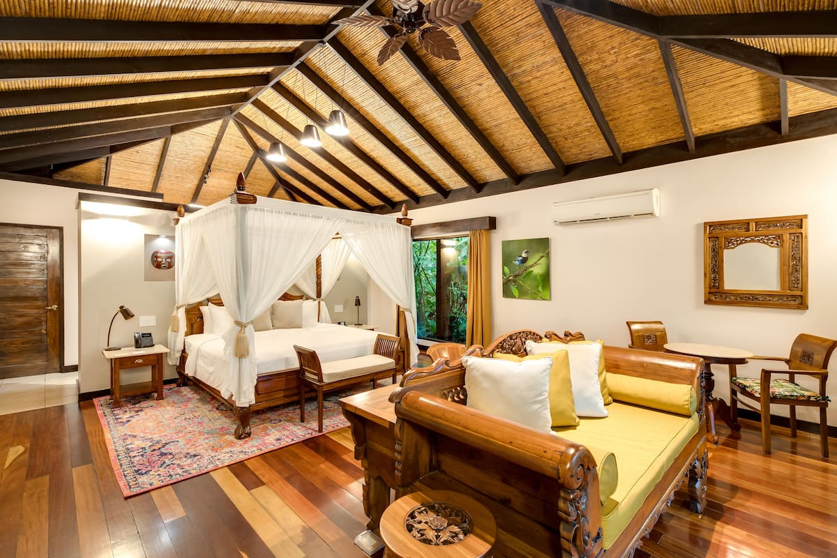 A spacious bedroom with a canopy bed, a wooden sofa, a dining table, and a small round table.