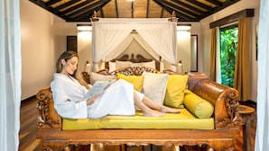 A person sitting on a wooden sofa with a canopy bed in the background.