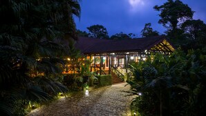 A well-lit building with a stone pathway leading to a wooden entrance, surrounded by lush tropical vegetation. - Hideaway Rio Celeste (Katira)