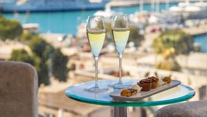 Una mesa con dos copas de vino blanco y pasteles, con vistas a un puerto deportivo lleno de barcos.