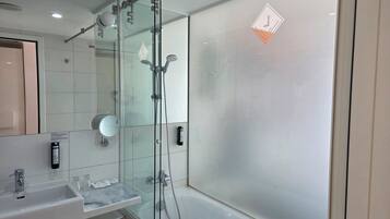 Un baño moderno con ducha de vidrio, lavamanos con espejo e inodoro.