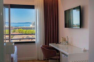 Ein Hotelzimmer mit großem Fenster und Blick auf ein Kreuzfahrtschiff und die Skyline der Stadt.