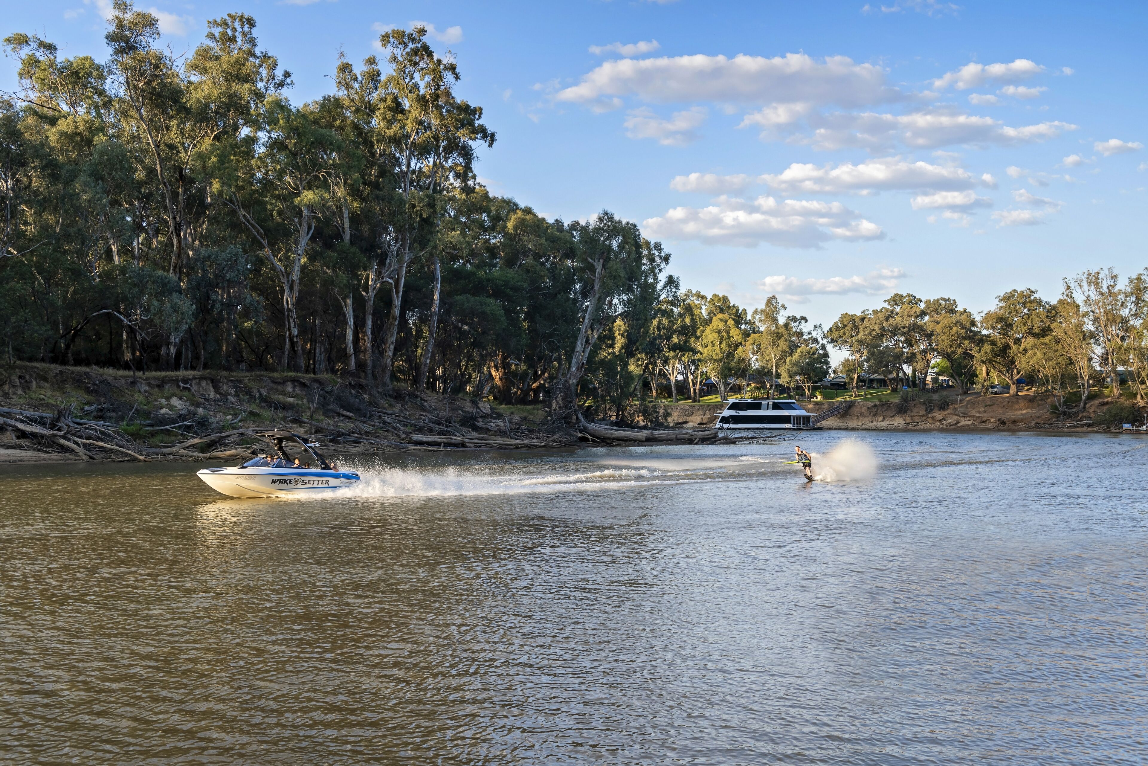 A boat on a river with a person wakeboarding behind it.