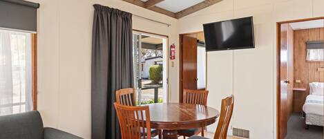 A dining area with a round wooden table and four chairs, a grey sofa, and a TV mounted on the wall.