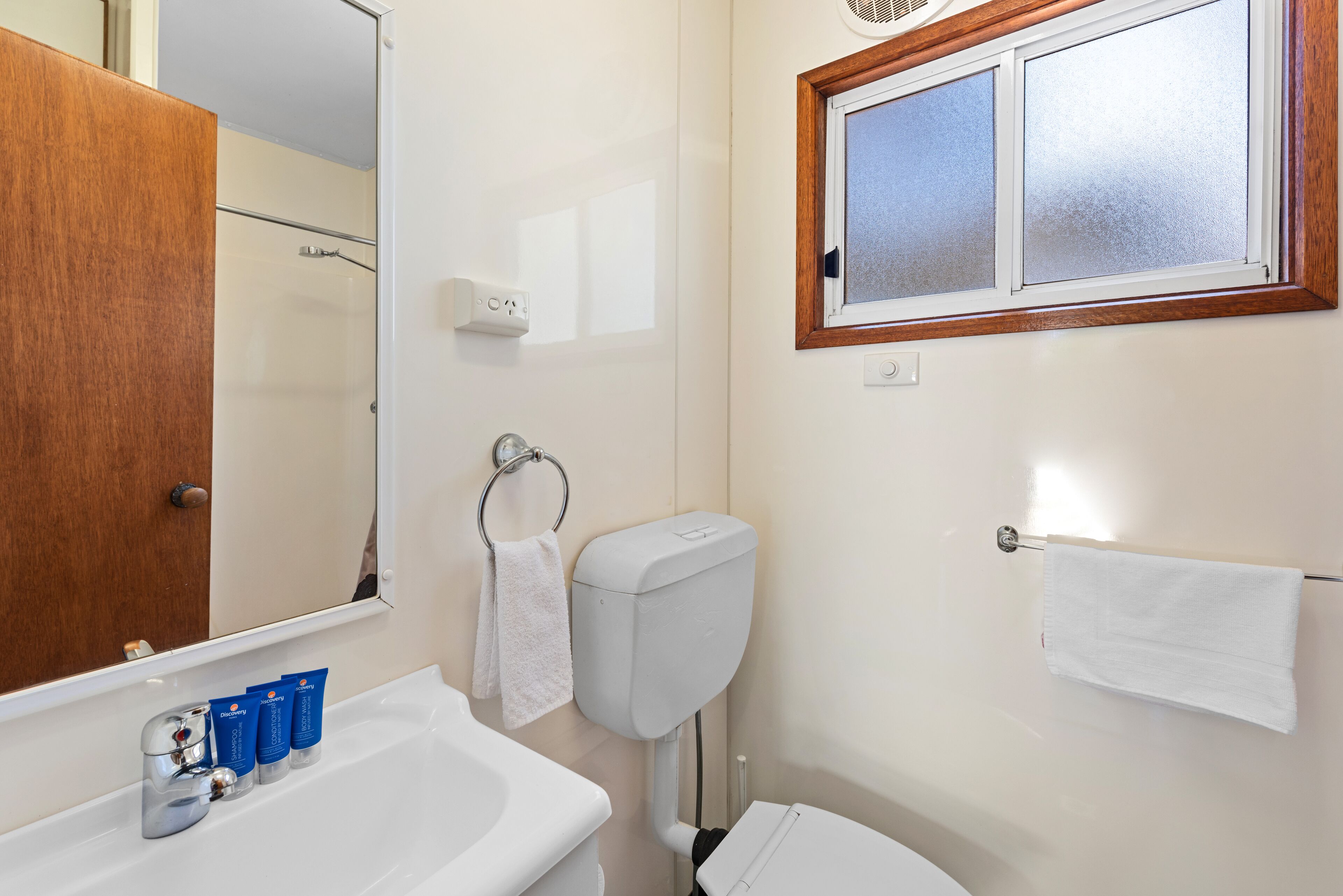 Un baño con lavamanos, espejo, inodoro y ventana.