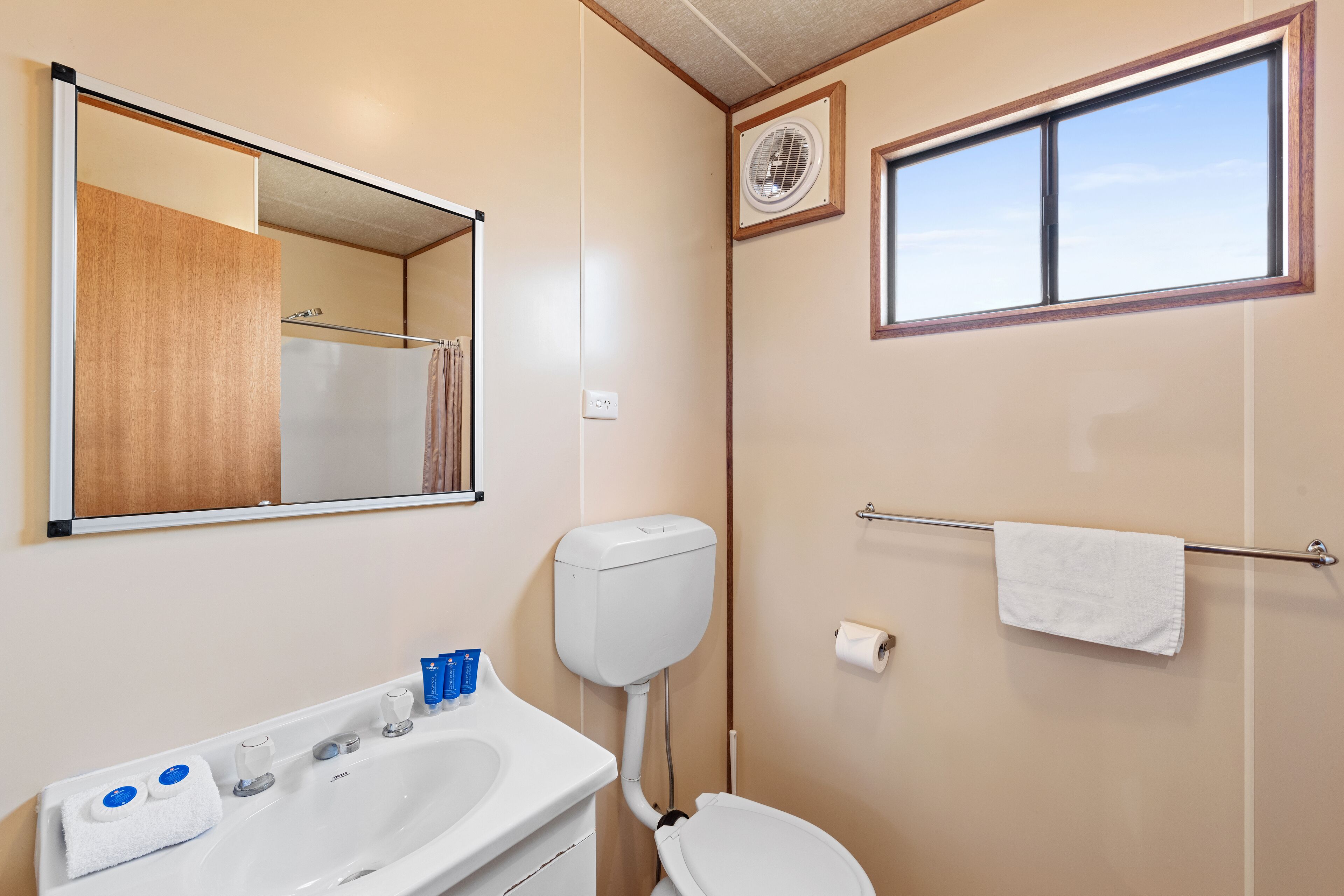 A bathroom with a sink, mirror, toilet, towel rack, and a window.