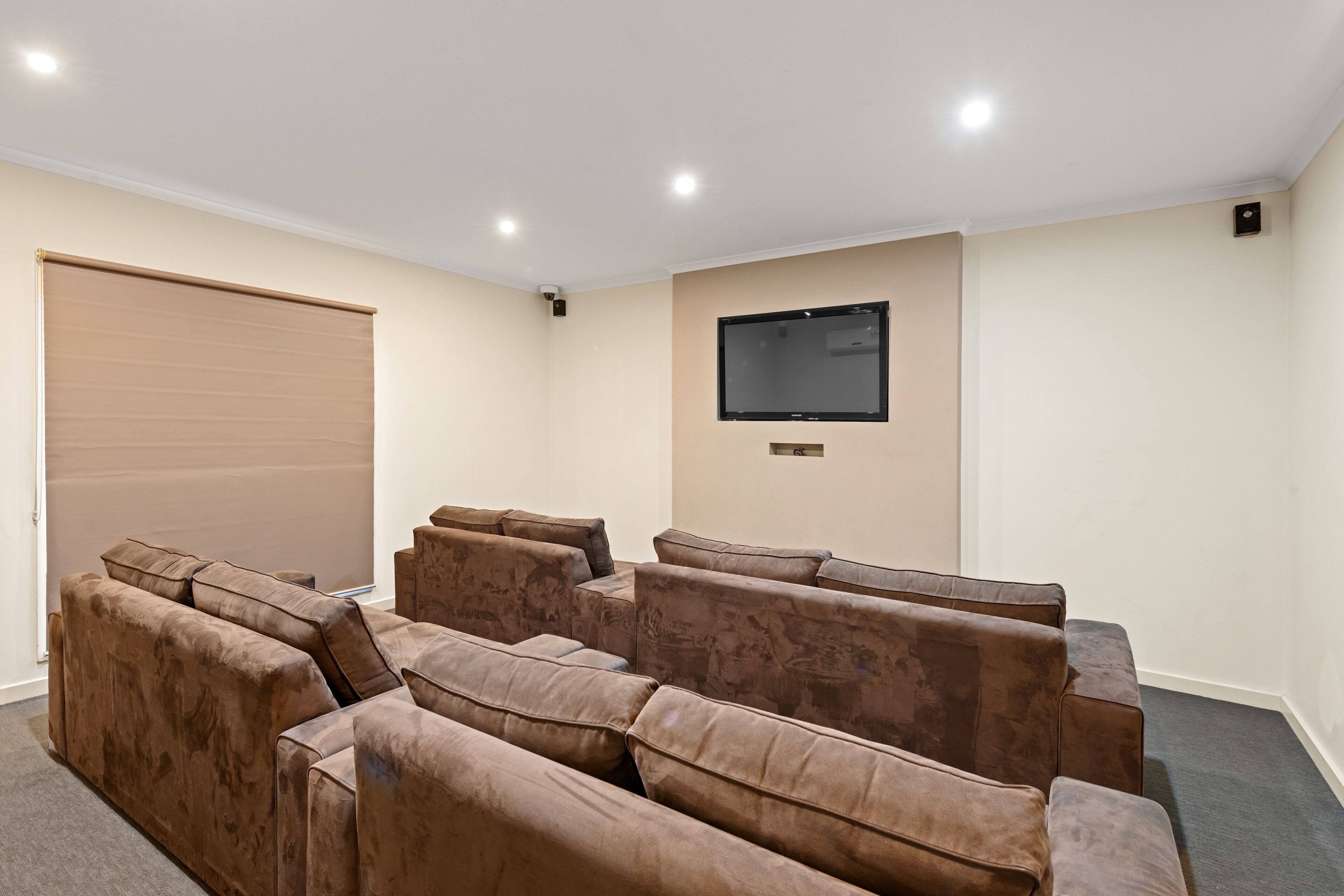 Una sala de cine en casa con una pantalla grande, varios espacios de descanso y una puerta corrediza cerrada.