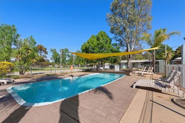 A rectangular swimming pool with a yellow shade sail overhead, surrounded by lounge chairs and a paved deck. - Discovery Parks - Moama West (Moama)