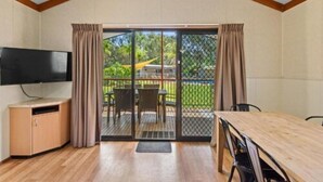 A room with a TV, a wooden table, and a sliding glass door leading to an outdoor area with chairs and a yellow hammock. - Discovery Parks - Moama West (Moama)