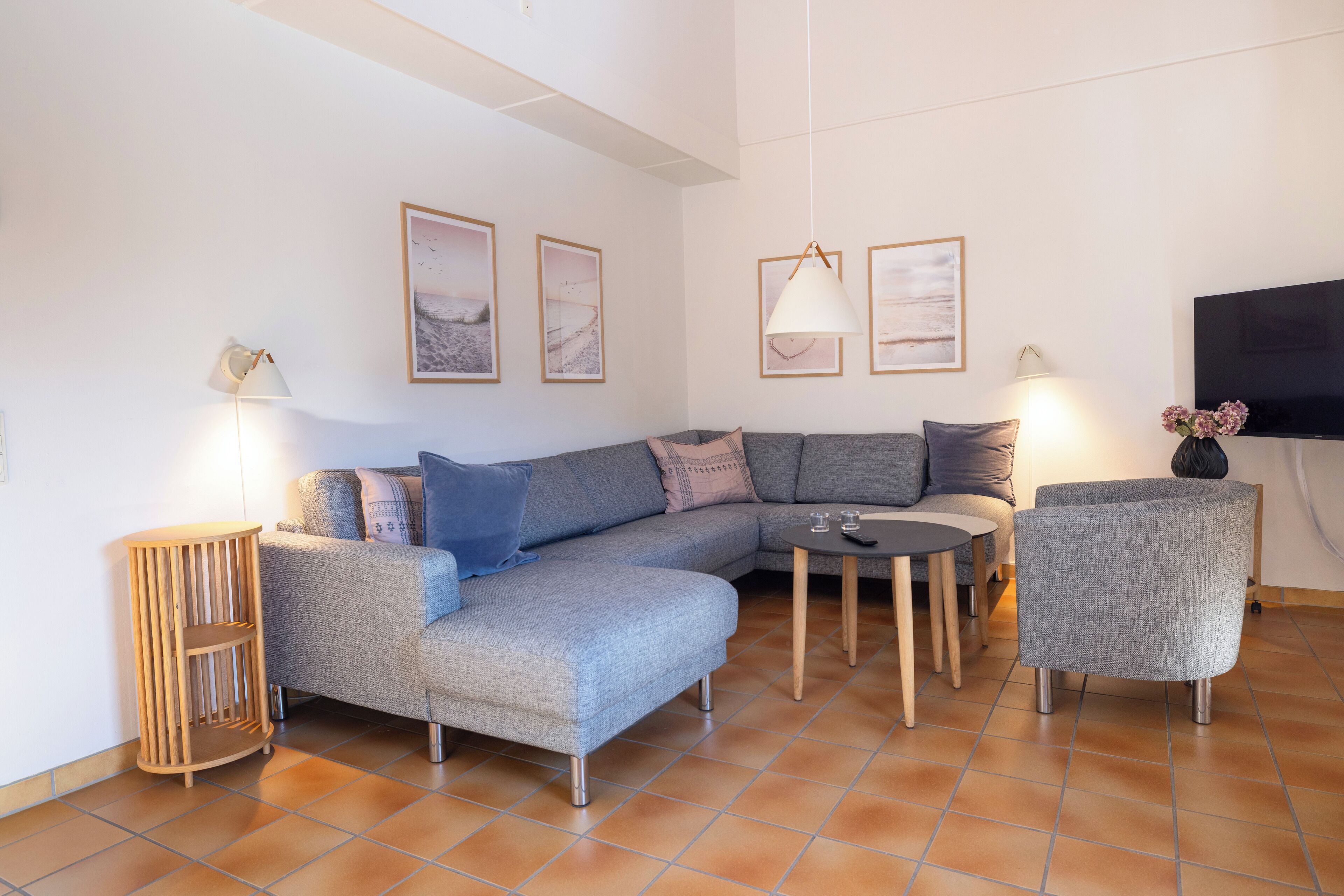 Een moderne woonkamer met een grijze modulaire bank, een klein rond tafeltje, een grijze fauteuil en een aan de muur bevestigde televisie.