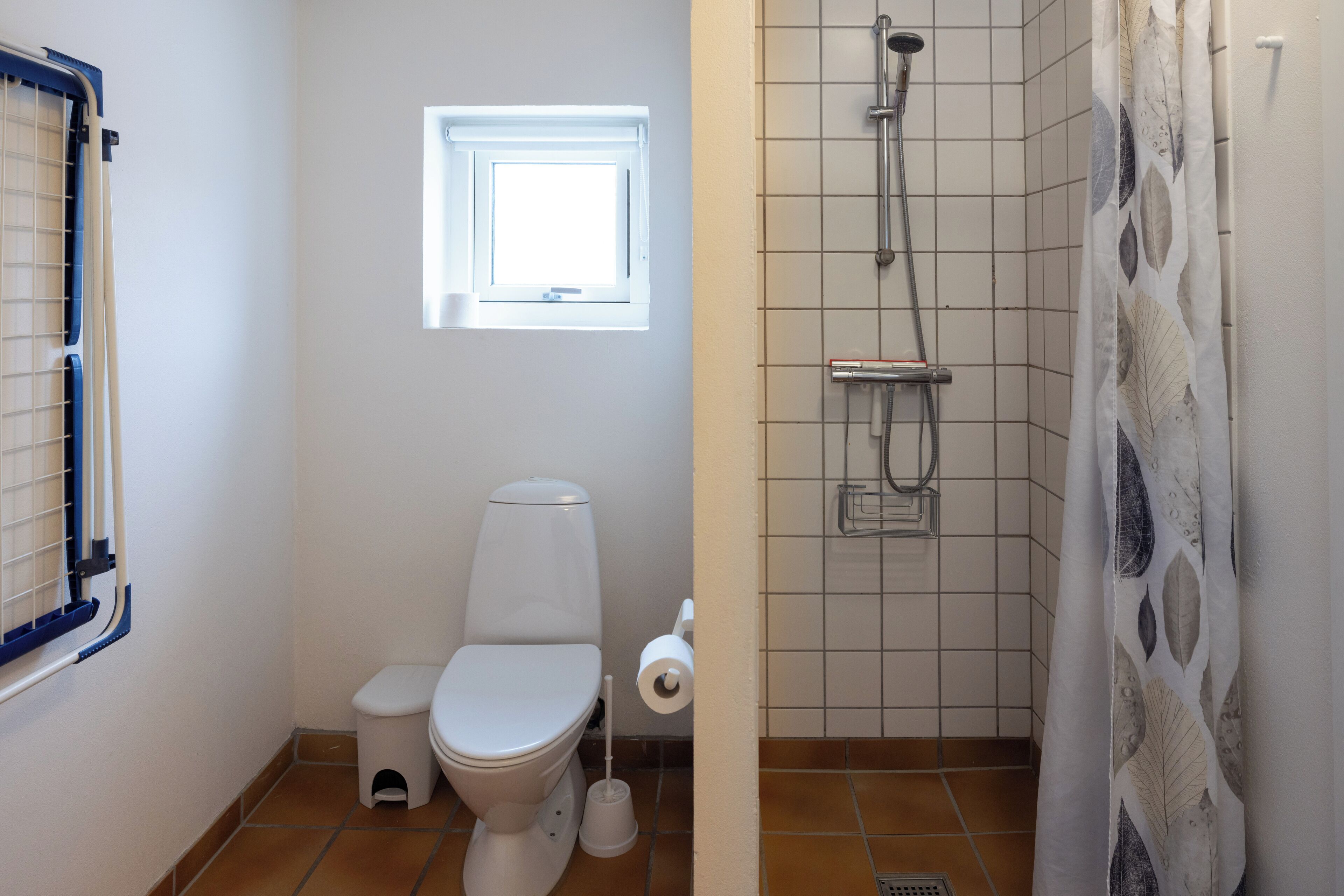 Une salle de bain équipée de toilettes, d’une fenêtre, d’une douche et d’un porte-rouleau de papier toilette.