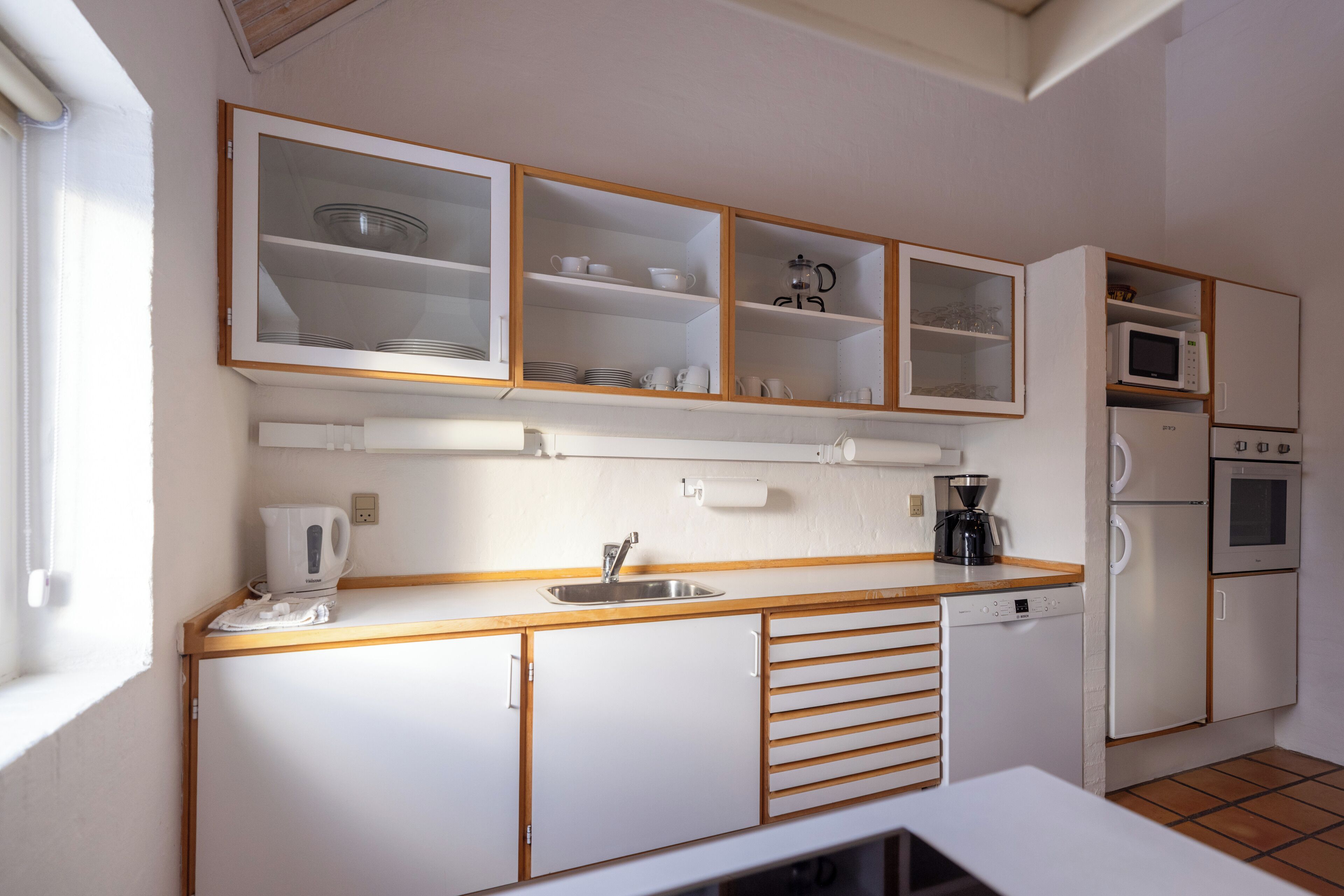 A compact kitchen with white cabinets, a built-in microwave, a coffee maker, and a dishwasher.
