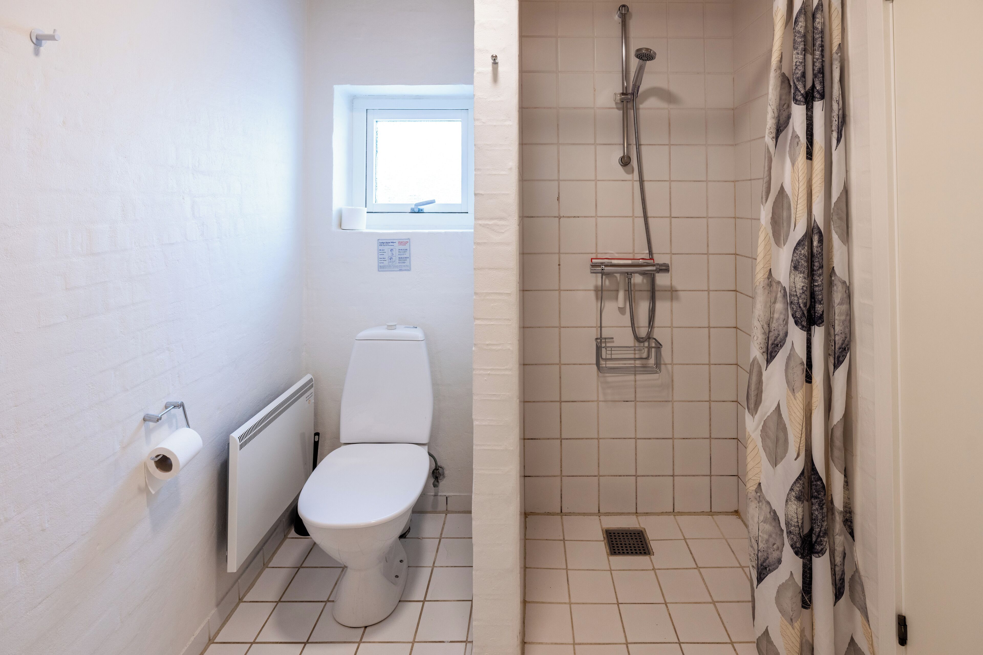 A bathroom with a toilet, a window, and a shower area.