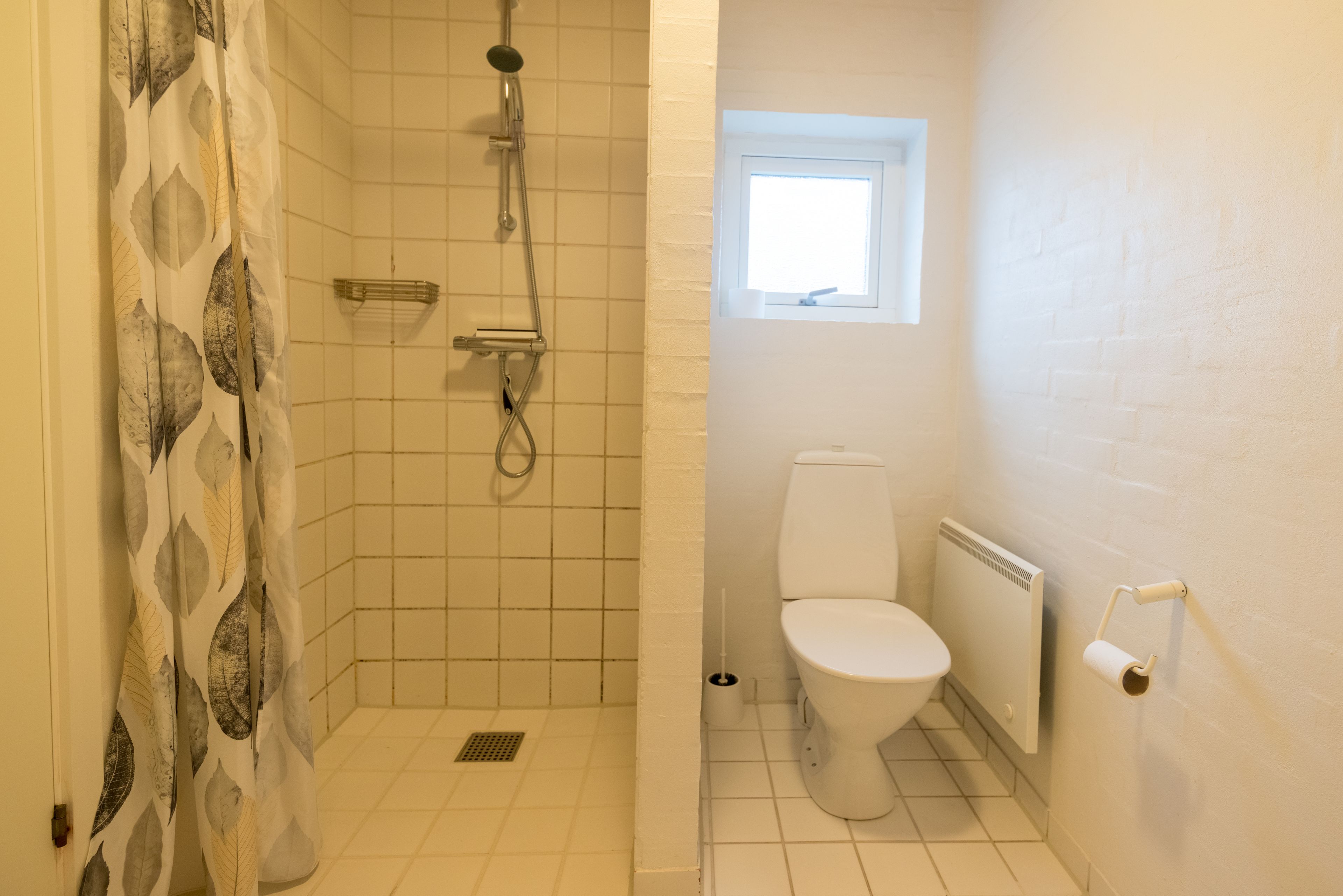 A bathroom with a shower, toilet, and a window.