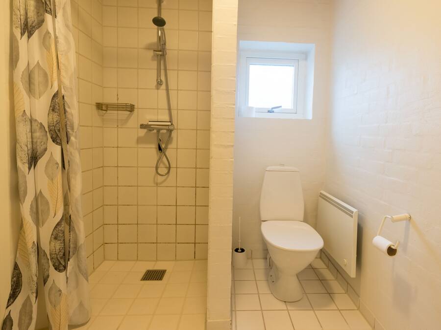 A bathroom with a shower, toilet, and a window.
