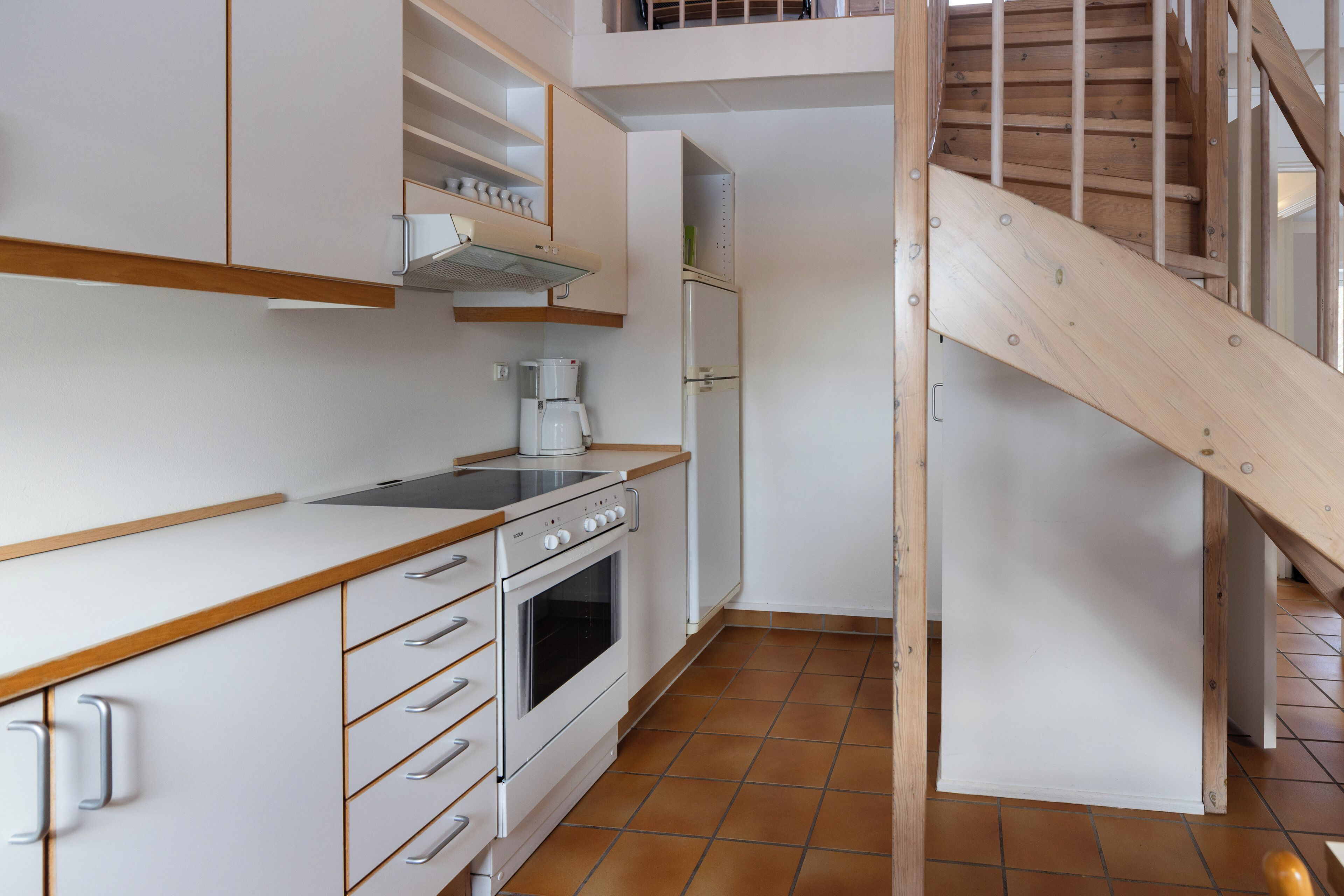 Une cuisine avec des meubles blancs, un plan de travail en bois, une cuisinière et une machine à café.