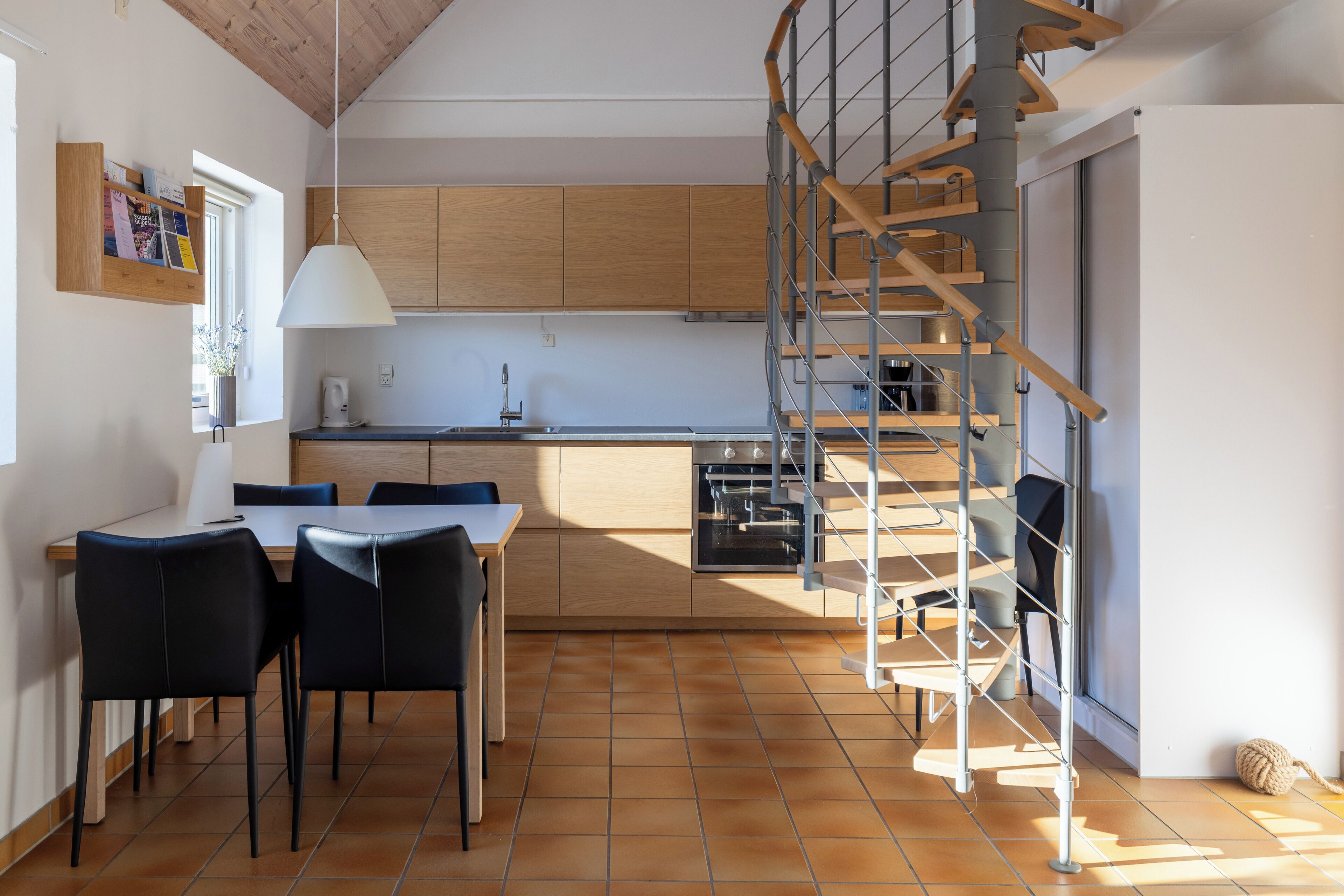 A modern kitchen with wooden cabinets, a dining table with chairs, and a spiral staircase.