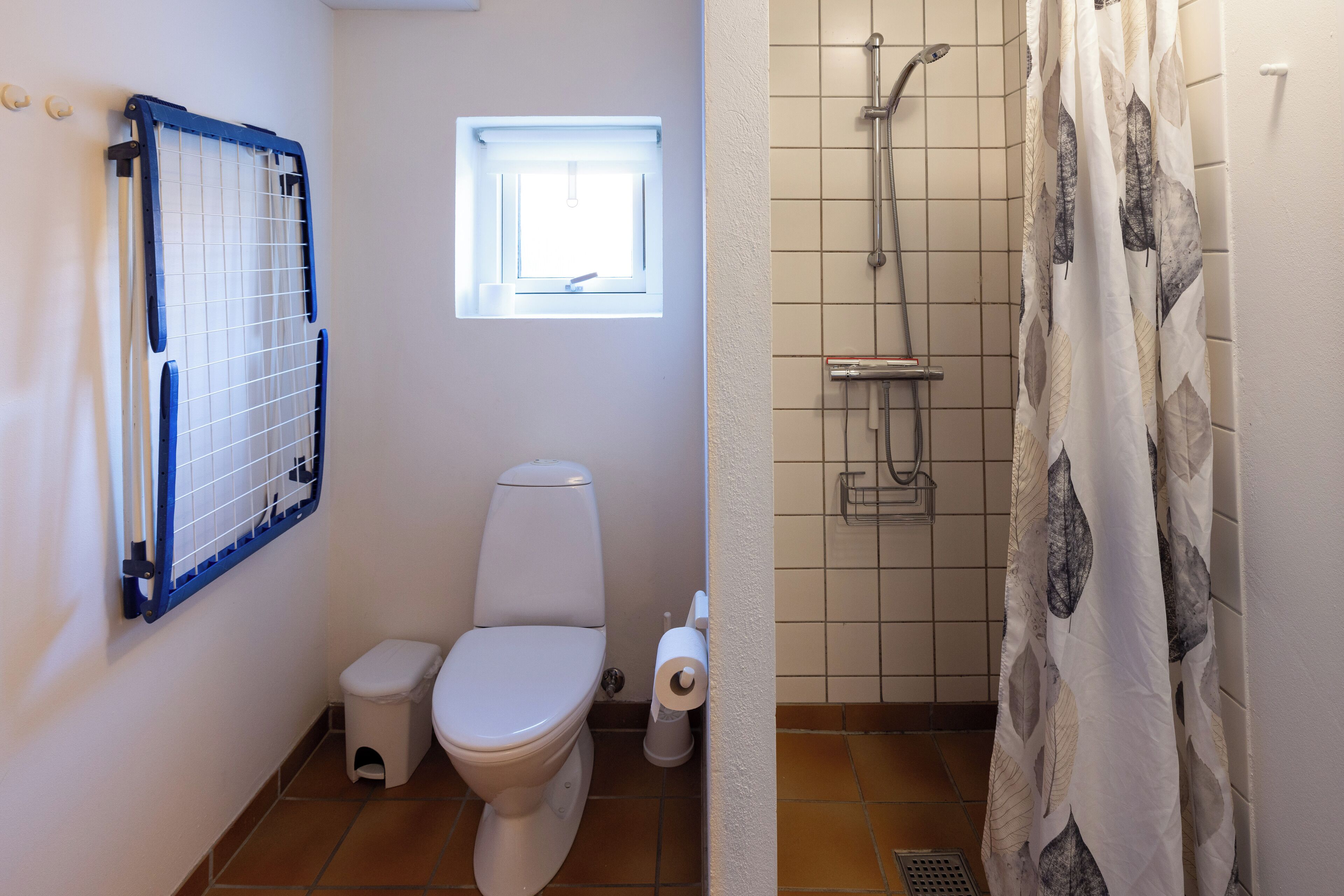 Une salle de bain comprenant des toilettes, une petite fenêtre, une douche avec un rideau et un porte-serviettes.