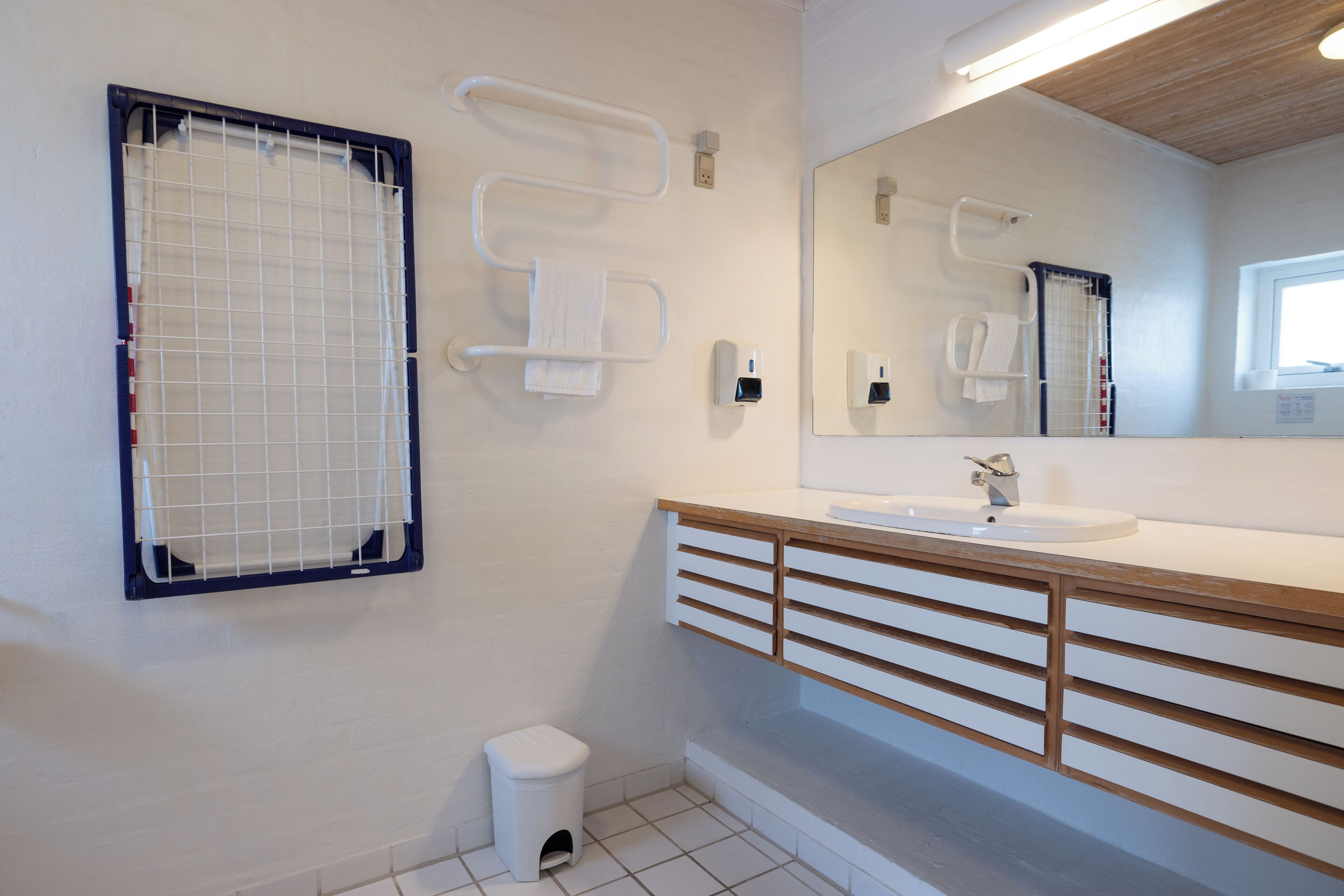Une salle de bain moderne avec un lavabo blanc, un meuble-lavabo en bois, des porte-serviettes et une fenêtre.