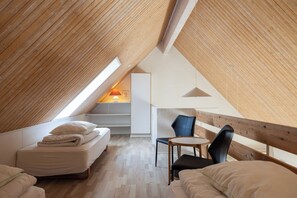 Ein gemütliches Schlafzimmer im Dachgeschoss mit schrägen Wänden, einem Bett, einem Sessel und einem kleinen Tisch.