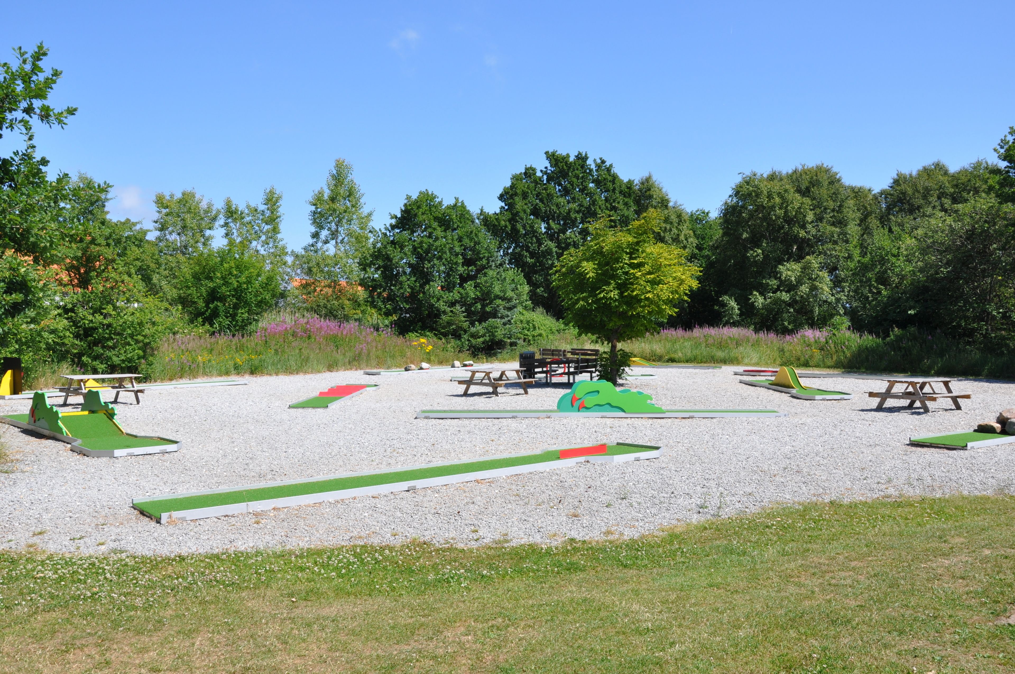 Une aire de jeux avec des structures colorées, vertes et rouges, des tables de pique-nique et des bancs.