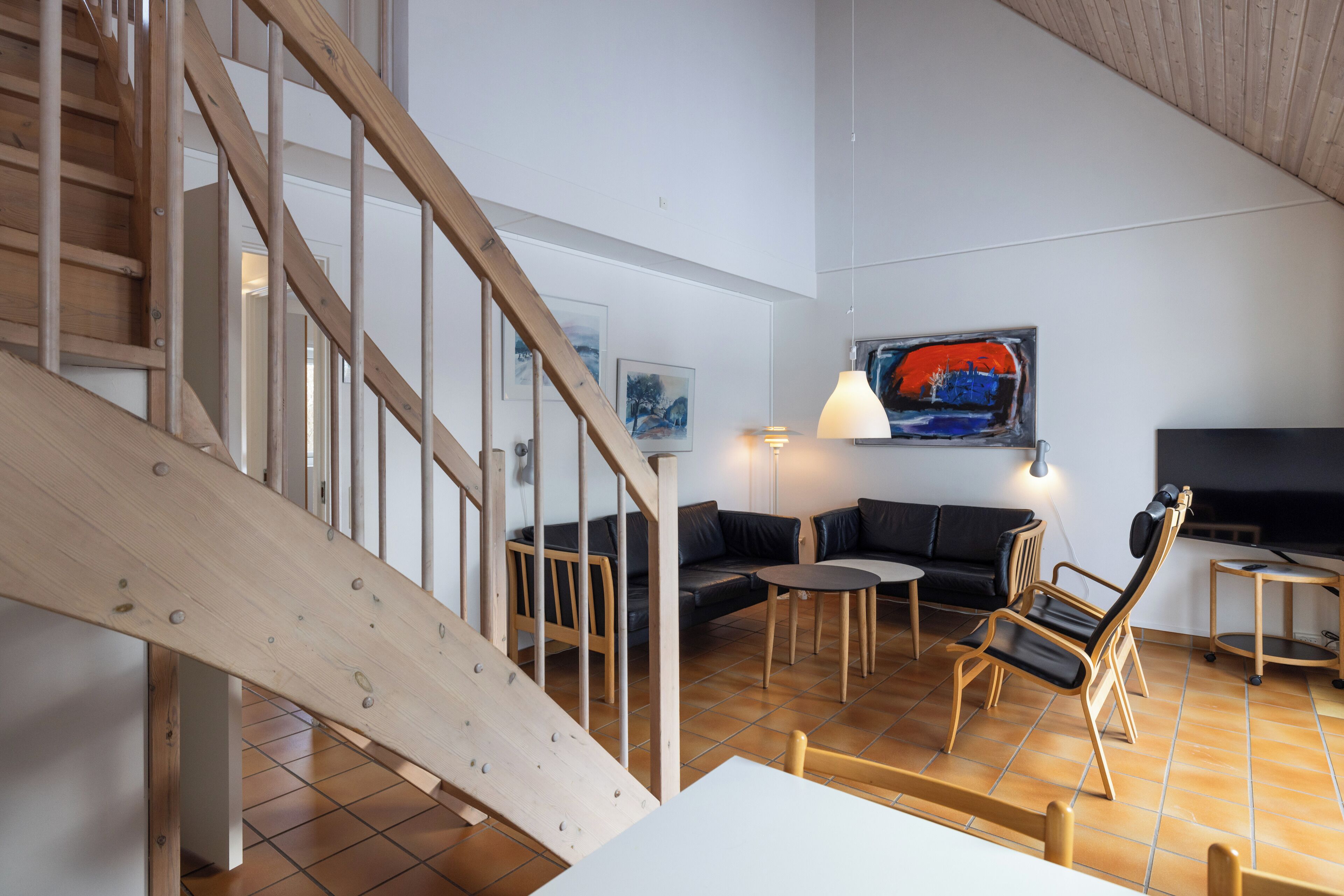 Un vaste espace de vie agrémenté d’un escalier en bois, d’un canapé en cuir noir, d’une table basse en bois et d’un tableau moderne accroché au mur.