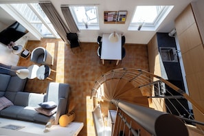 A modern interior with a dining area, a staircase, and a living room with a sofa and a TV.