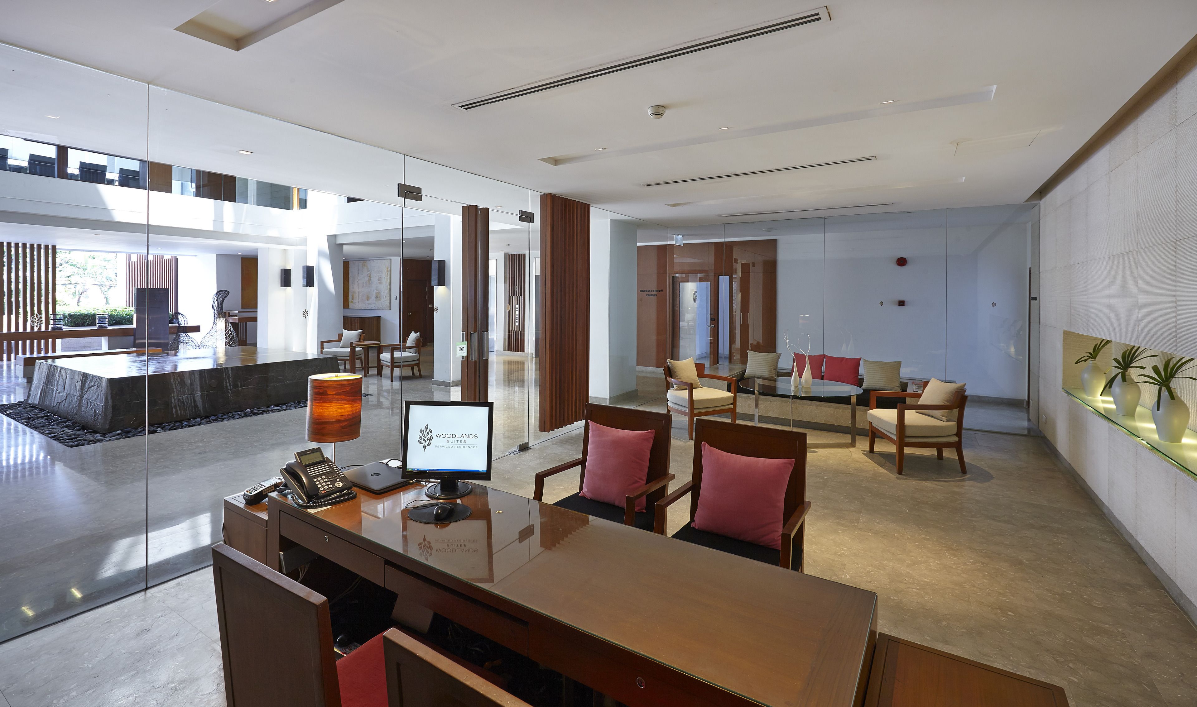 A modern hotel lobby with a reception desk, seating area, and a large glass wall offering a view of the outdoor area.