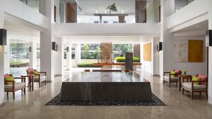 A spacious lobby with a central water feature, seating areas, and a view of the outdoors. - Woodlands Suites Serviced Residences (Pattaya)