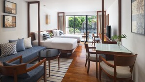A modern hotel room with a sofa, two beds, a dining table, and a large window offering a view of greenery. - Woodlands Suites Serviced Residences (Pattaya)