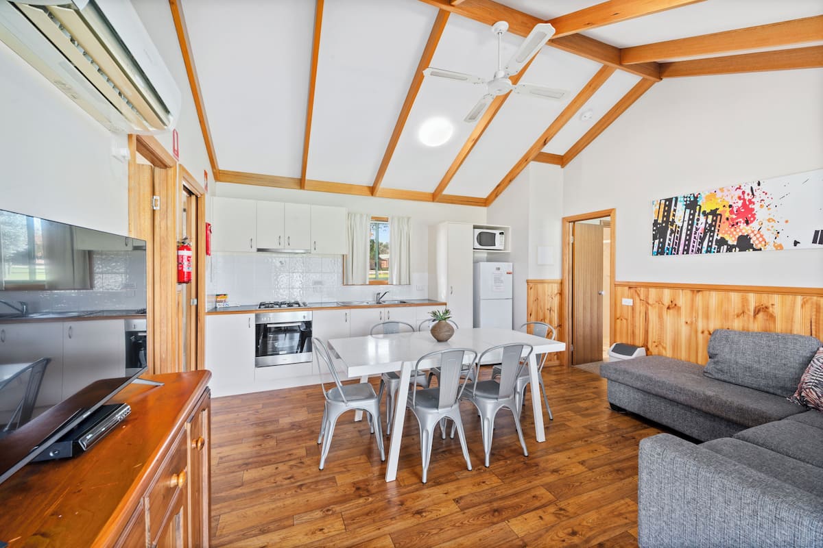 Una cocina moderna con armarios blancos, microondas y un comedor con mesa blanca y sillas grises.