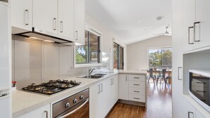 A modern kitchen with white cabinetry, a gas stove, and a large window. - Lake Hume Holiday Park (Bowna)