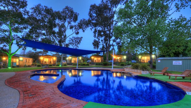 A swimming pool with a brick pathway, surrounded by trees and a shaded area. - Lake Hume Holiday Park (Bowna)