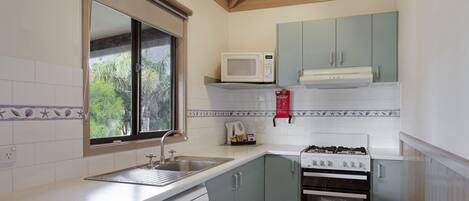 Cocina compacta equipada con lavavajillas, estufa, microondas y ventana con vistas a la vegetación.