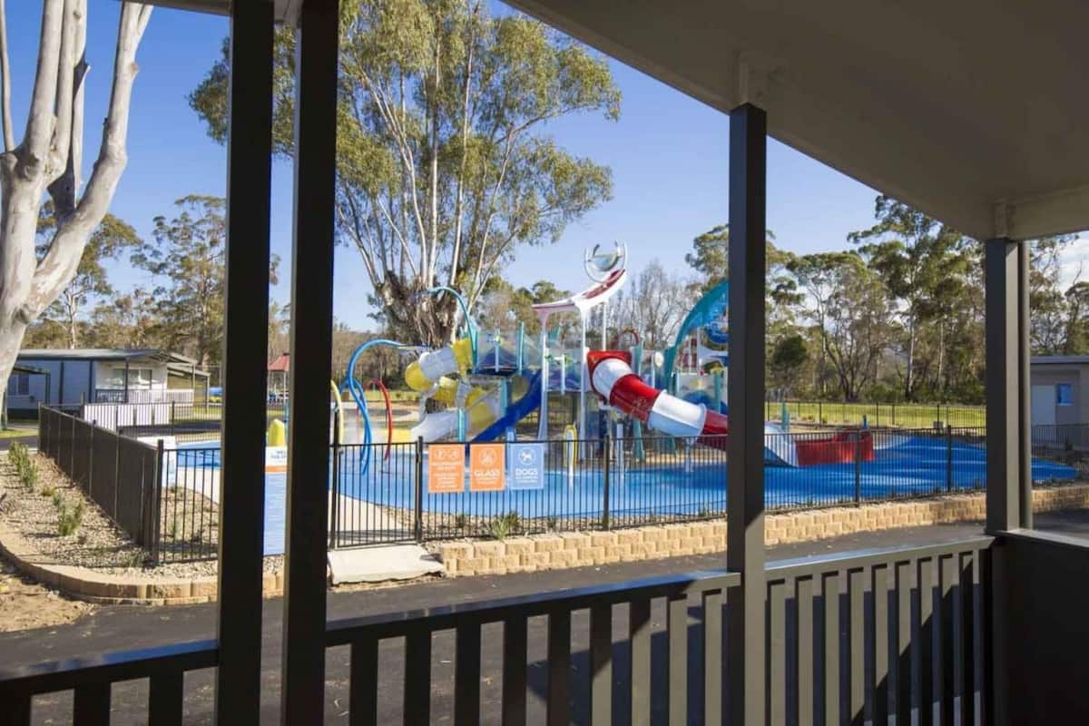A playground with slides and climbing structures, surrounded by trees and a fenced area.