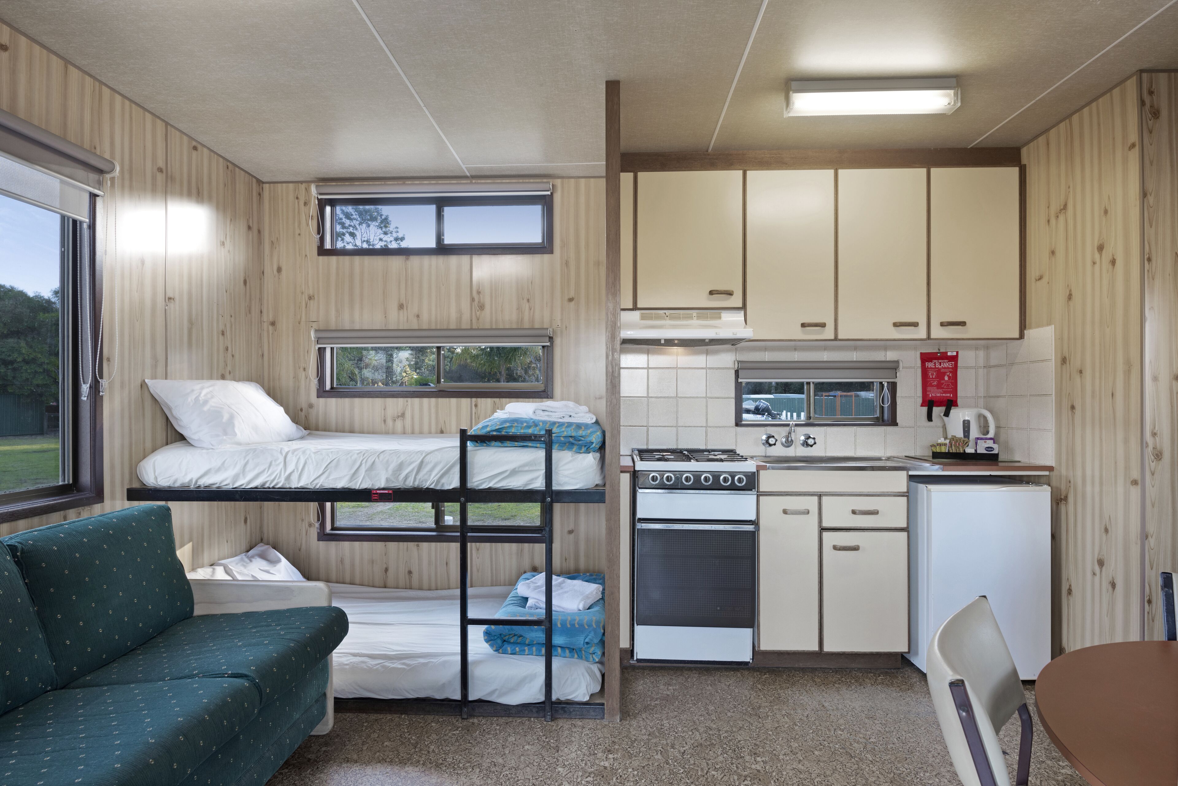 A compact room with bunk beds, a kitchenette, a small dining area, and a window providing a view of the outdoors.
