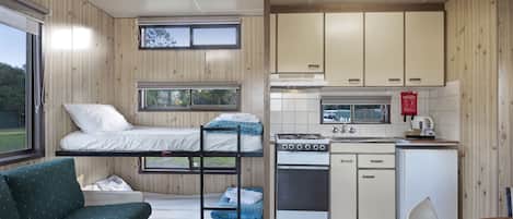 A compact room with bunk beds, a kitchenette, a small dining area, and a window providing a view of the outdoors.
