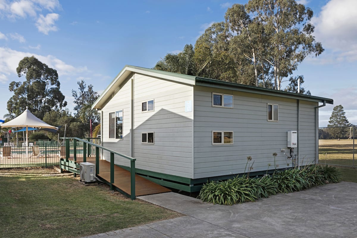 A single-story building with a green roof and white siding. It features a small porch with a wooden deck and a green railing.