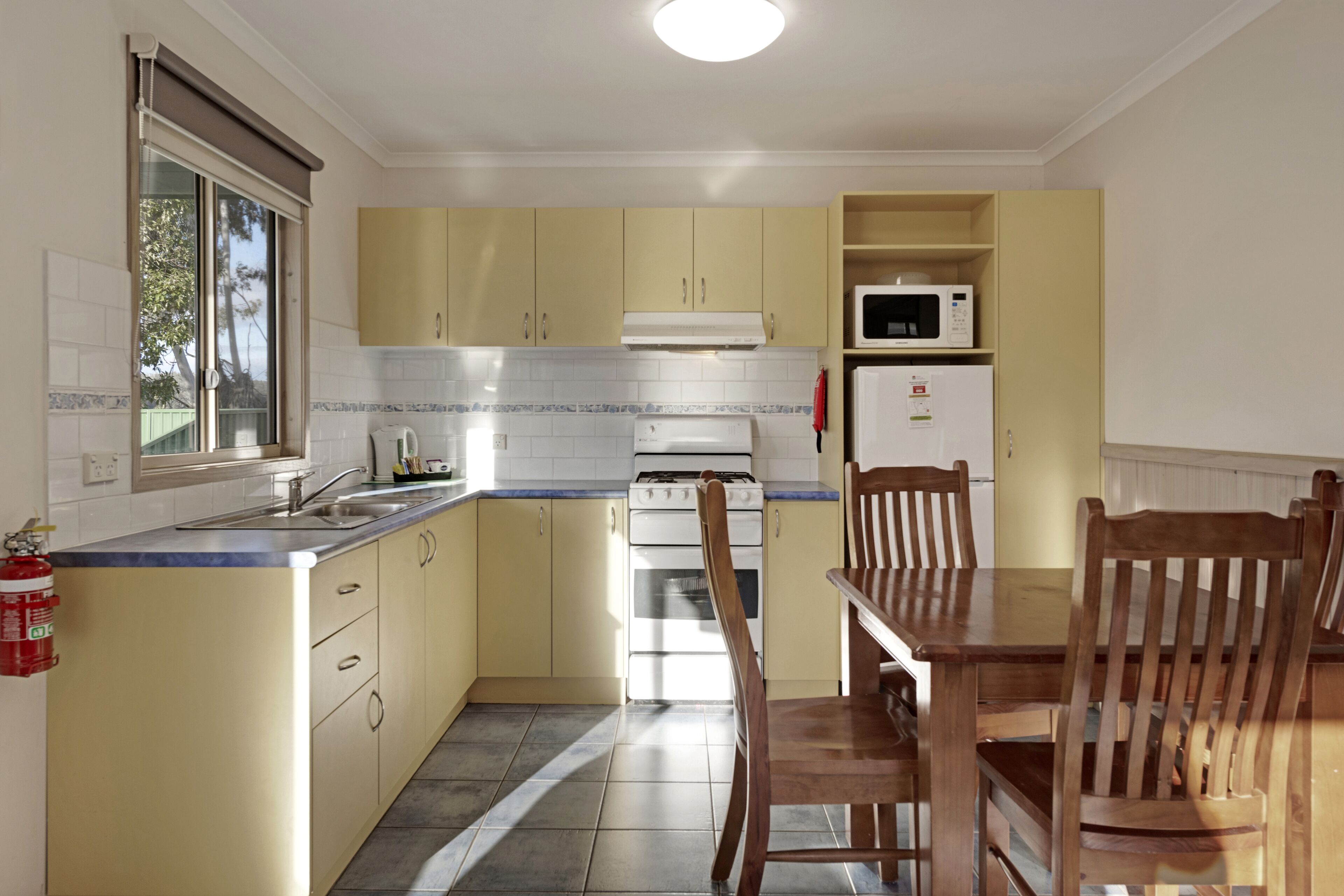 A compact kitchen with yellow cabinets, a white stove, a microwave, and a dining table with wooden chairs.