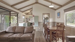 A cozy interior with a wooden dining table, cushioned seating, and a kitchen area in the background. - Discovery Parks - Eden (Boydtown)