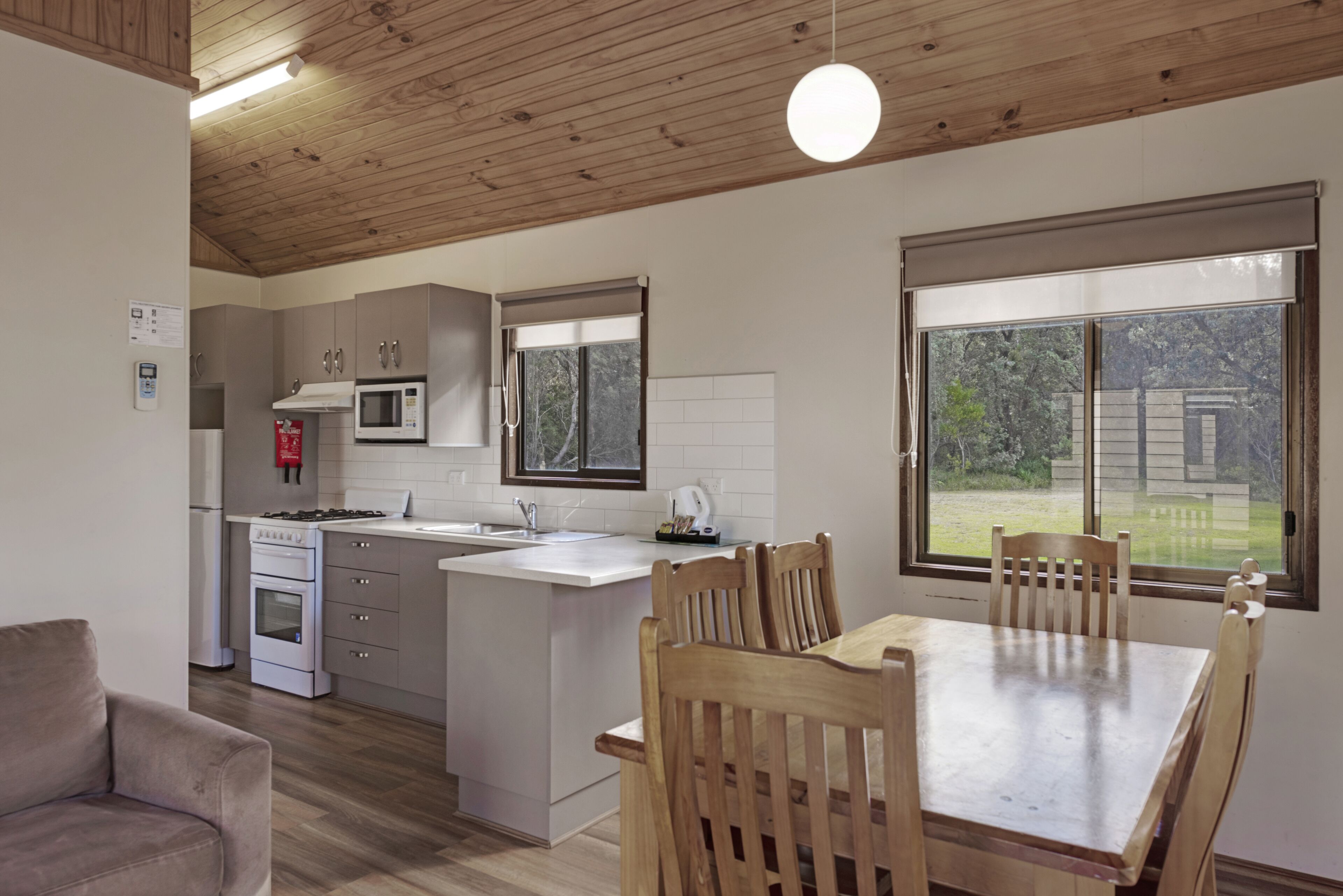 A modern kitchen with white cabinets, a microwave, and a stove. There is a dining area with a wooden table and chairs.