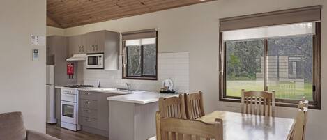A modern kitchen with white cabinets, a microwave, and a stove. There is a dining area with a wooden table and chairs.