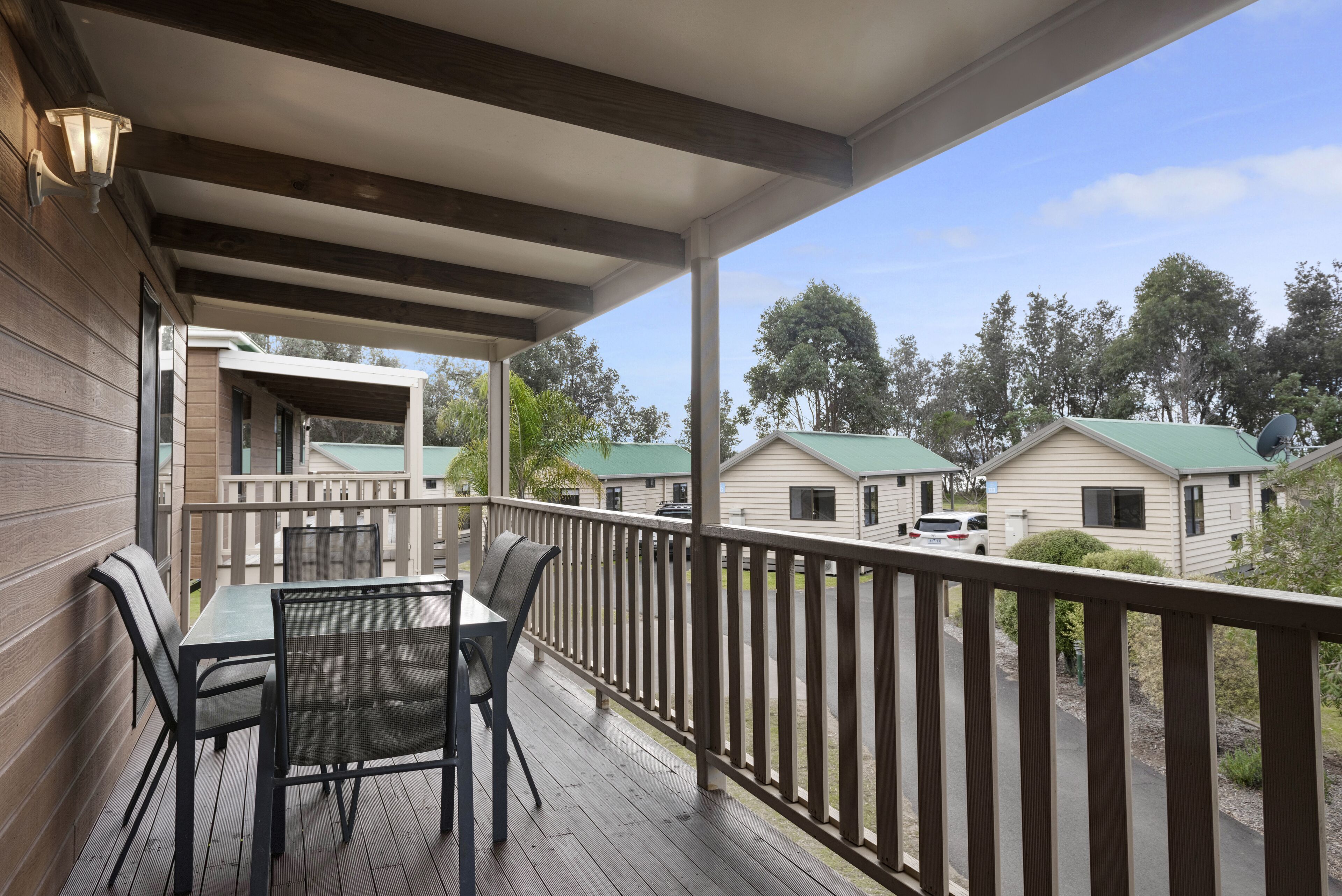 A covered outdoor area with a table and chairs, wooden railings, and a view of other buildings.